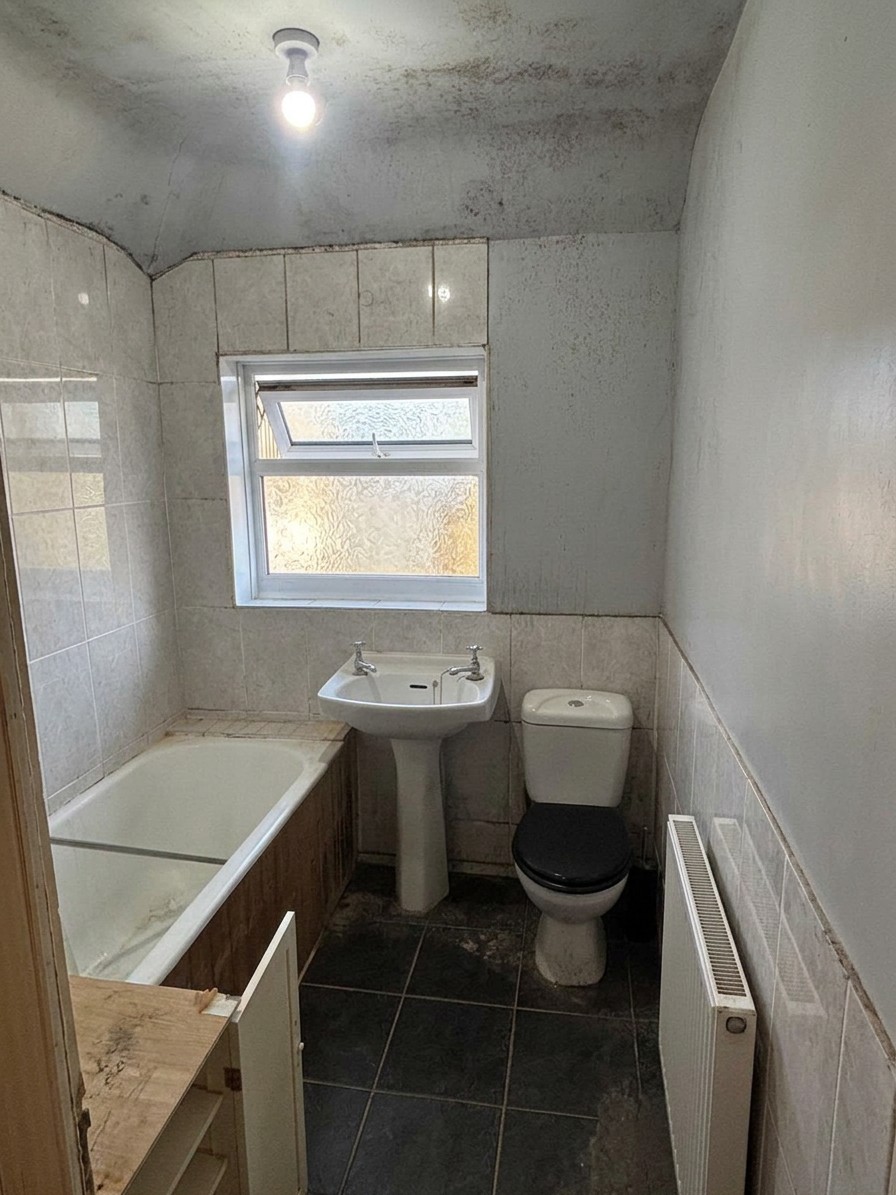 Dated bathroom with tired wall tiles, damp-stained ceiling, old bath, basin and toilet before renovation