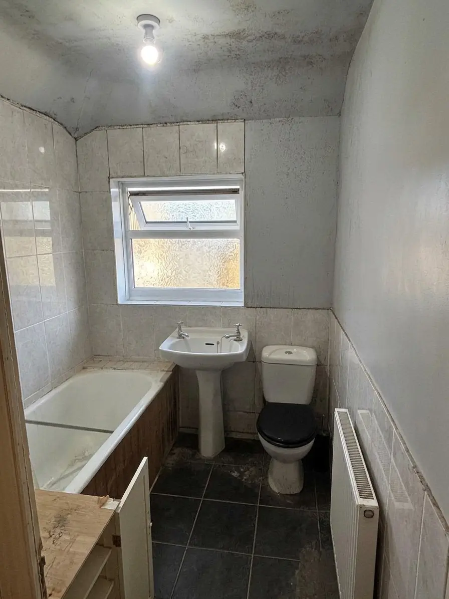Dated bathroom with tired wall tiles, damp-stained ceiling, old bath, basin and toilet before renovation