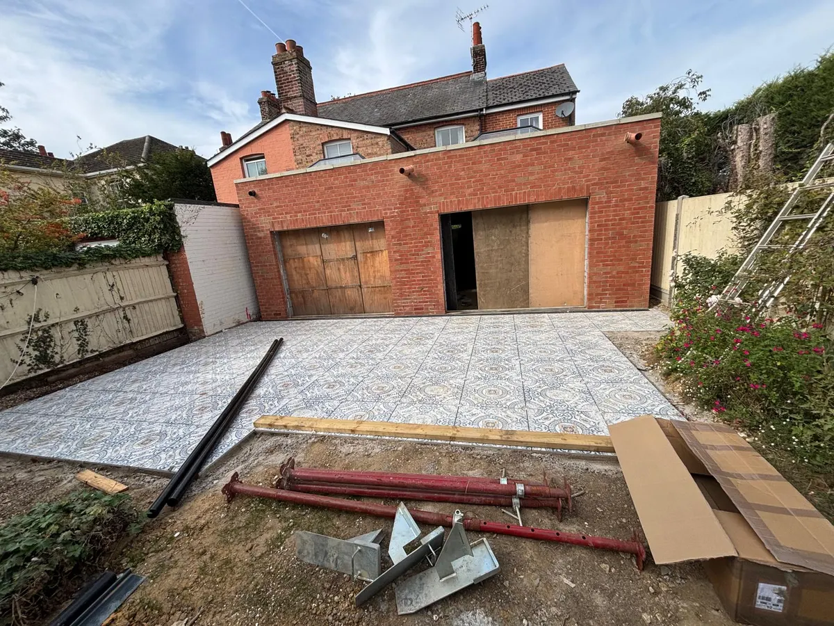 Rear of a red-brick house with a new flat-roofed single-storey brick extension, door openings boarded up and a freshly laid patterned patio in front