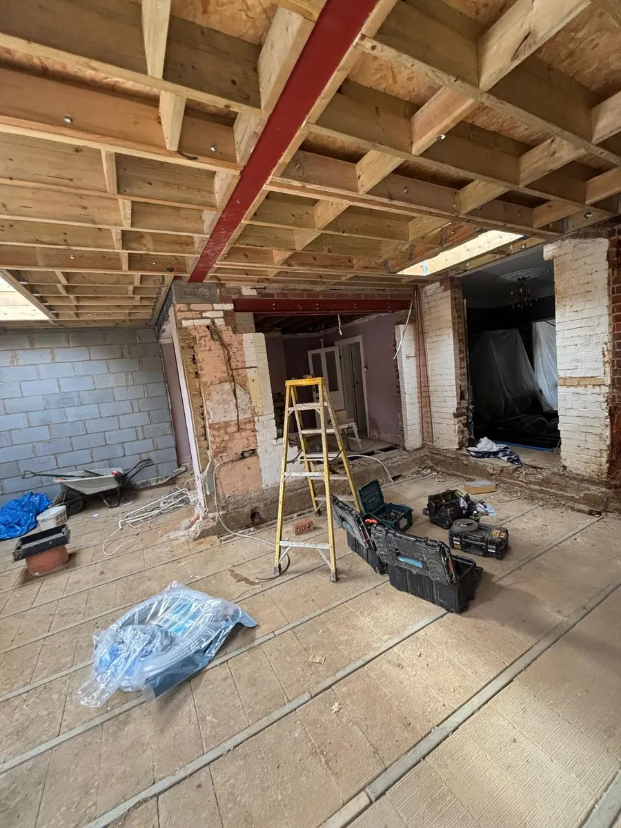 Back wall of the original house opened up beneath a red steel beam, looking through into the existing rooms