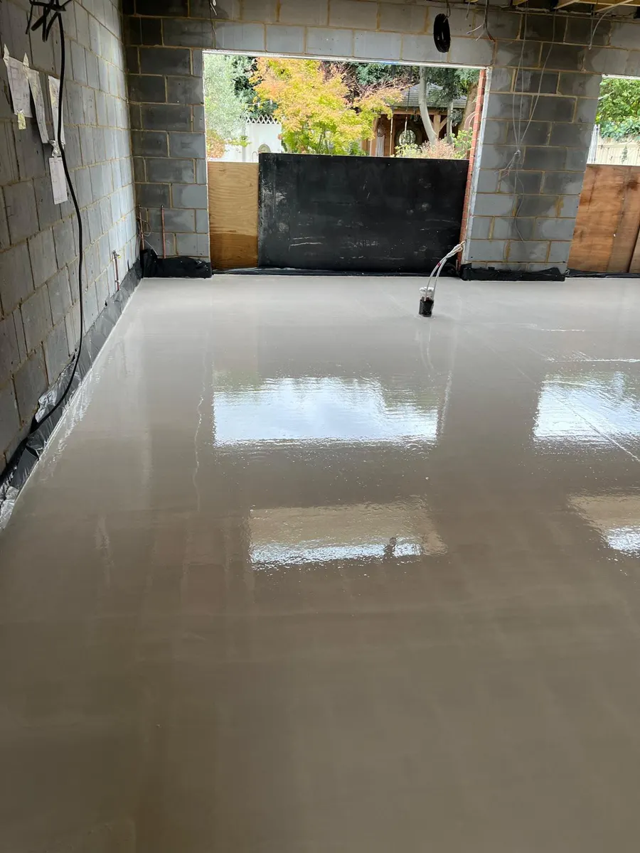Wet liquid screed floor across the extension with blockwork walls and the garden visible through the door opening