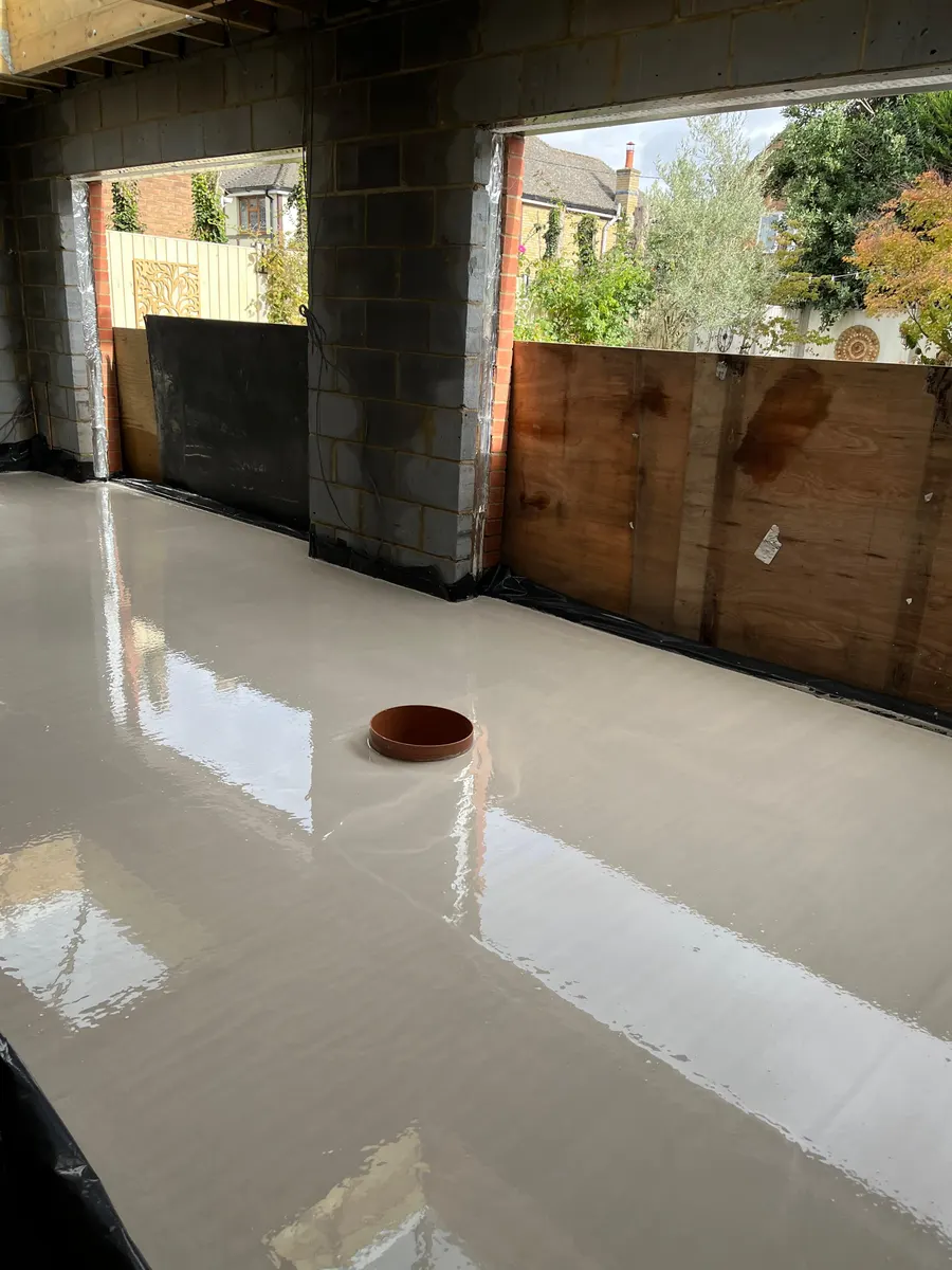 Freshly poured liquid screed floor in the extension, glossy and level, with the boarded door openings behind