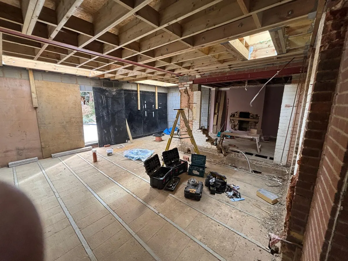 Inside the extension shell: exposed timber roof joists, rooflight opening, red steel beams and the back wall of the house opened up